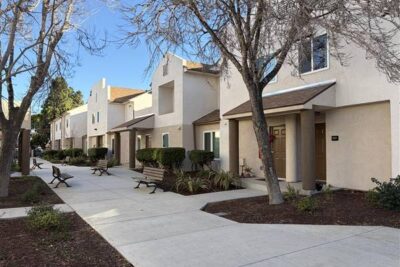 Sidewalk path with benches and trees next to apartment complex.