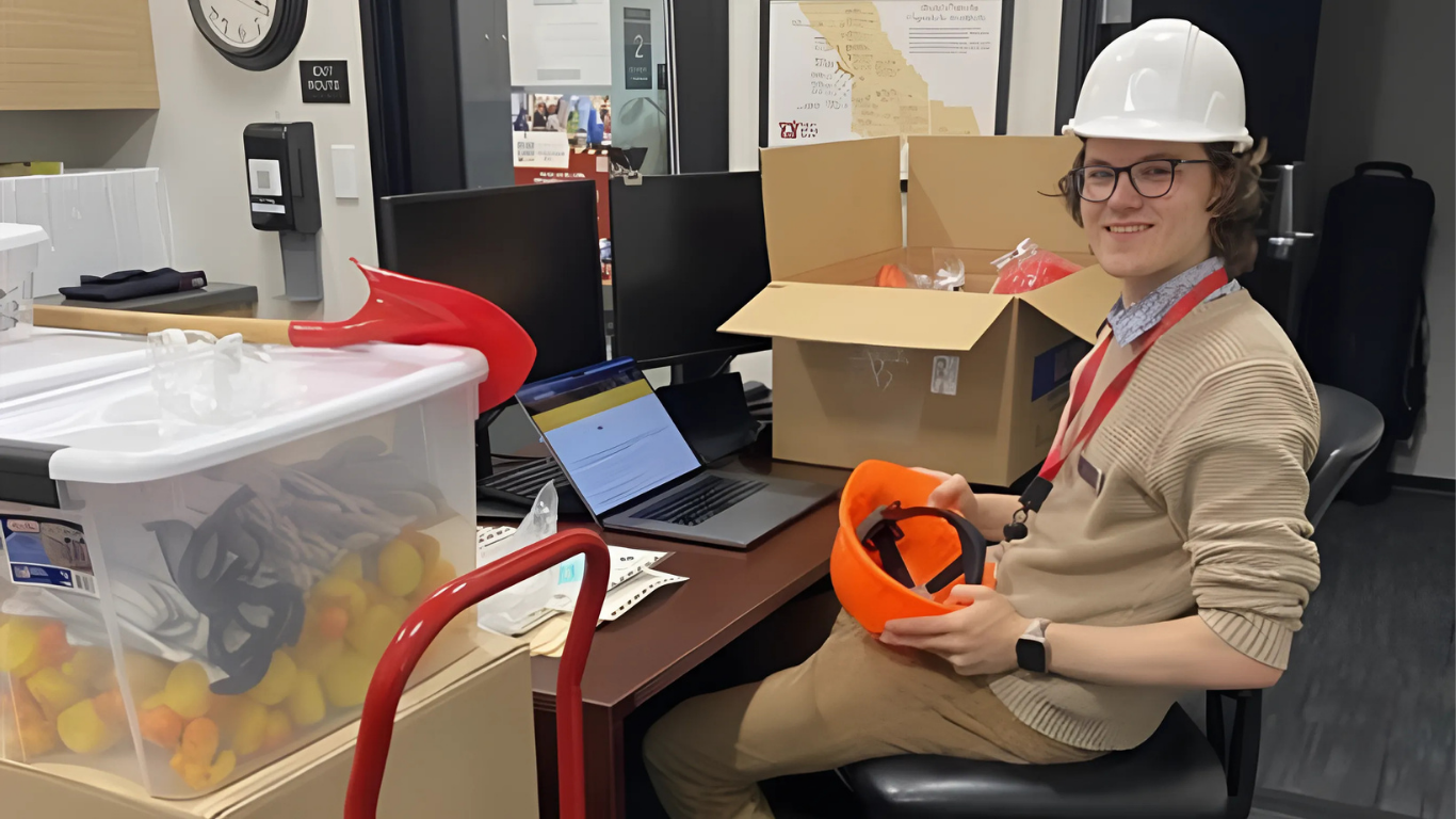 Man with white hard hat holds orange hard hat while smiling at the camera
